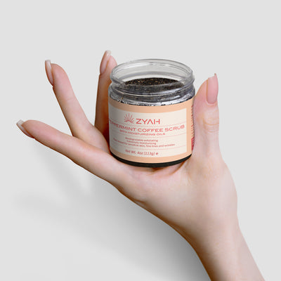 Hand holding a jar of ZYAH peppermint coffee scrub Botanical Skincare against a light background